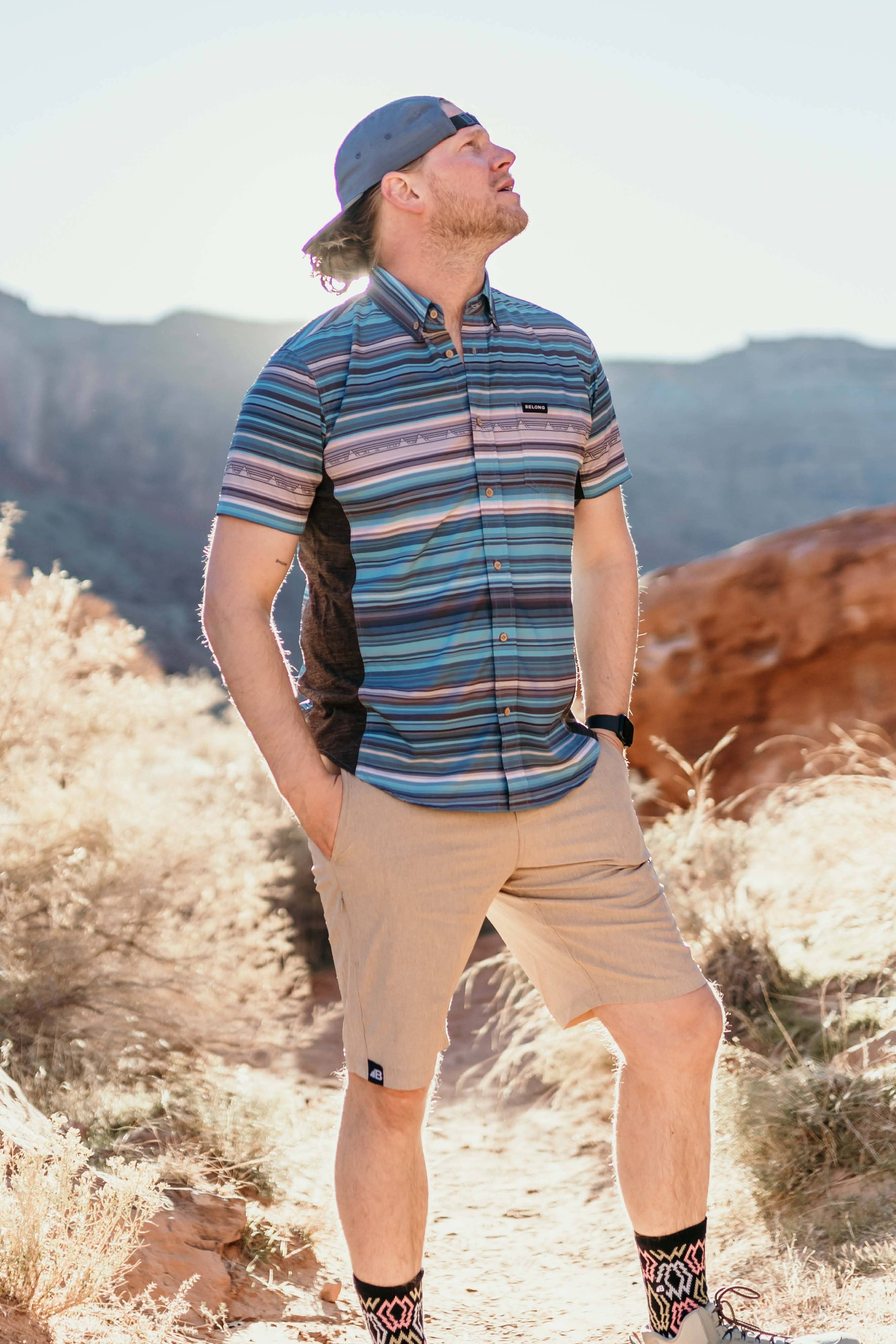 The Vista Stretch Button Down from Belong Designs features a modern, casual design in Summit Teal. This short-sleeve shirt includes a buttoned-down collar and is crafted from wrinkle-resistant fabric. It also comes with a small chest pocket adorned with a logo patch reading "Belong Designs.