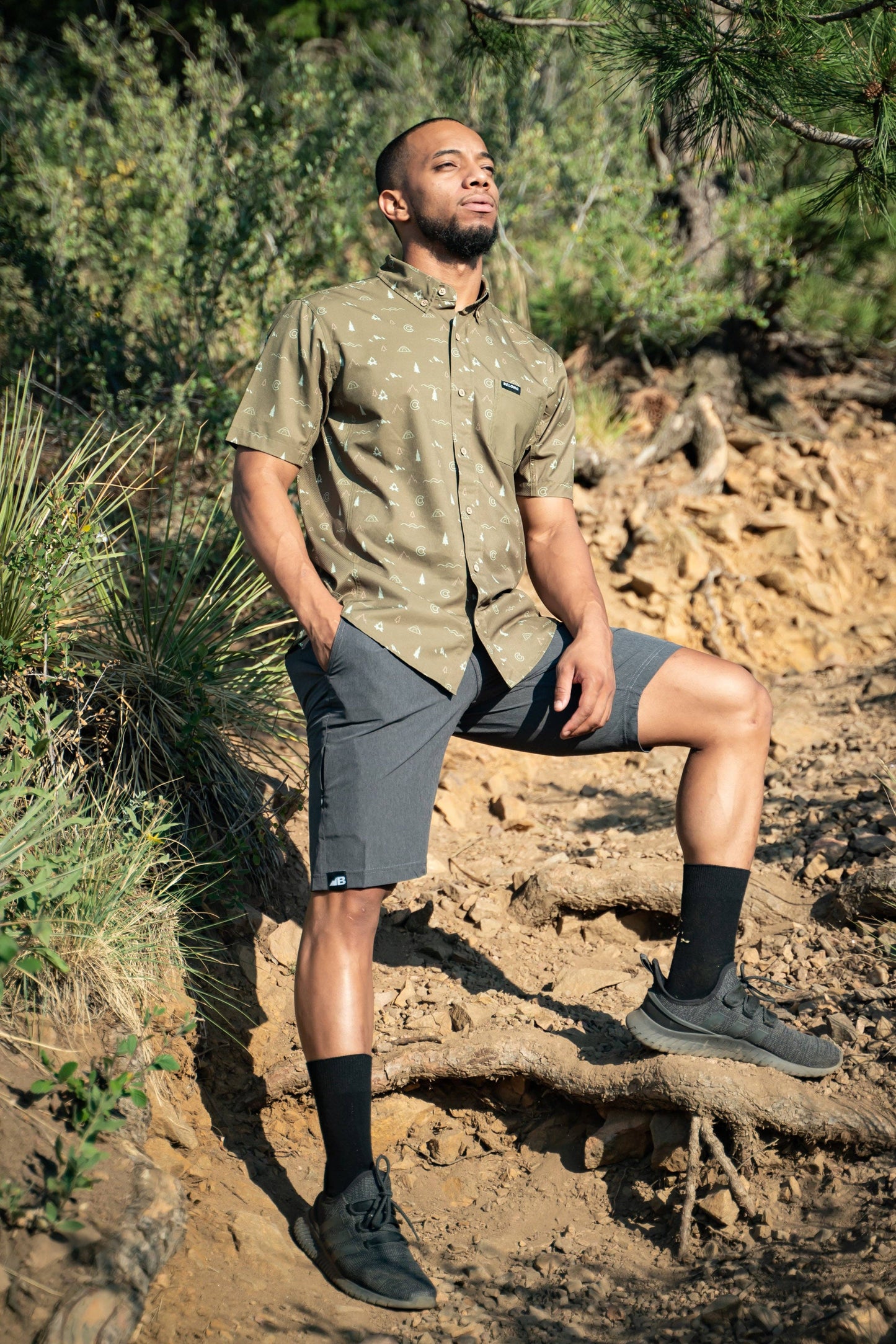 Introducing the Men's 10" Rocky Mountain Board Shorts by Belong Designs: a pair of gray knee-length shorts crafted from Venterrex material for quick dry technology. These shorts feature a subtle texture, a black drawstring on the waistband, side pockets, and a small black logo tag with white "MB" letters on the front left hem.