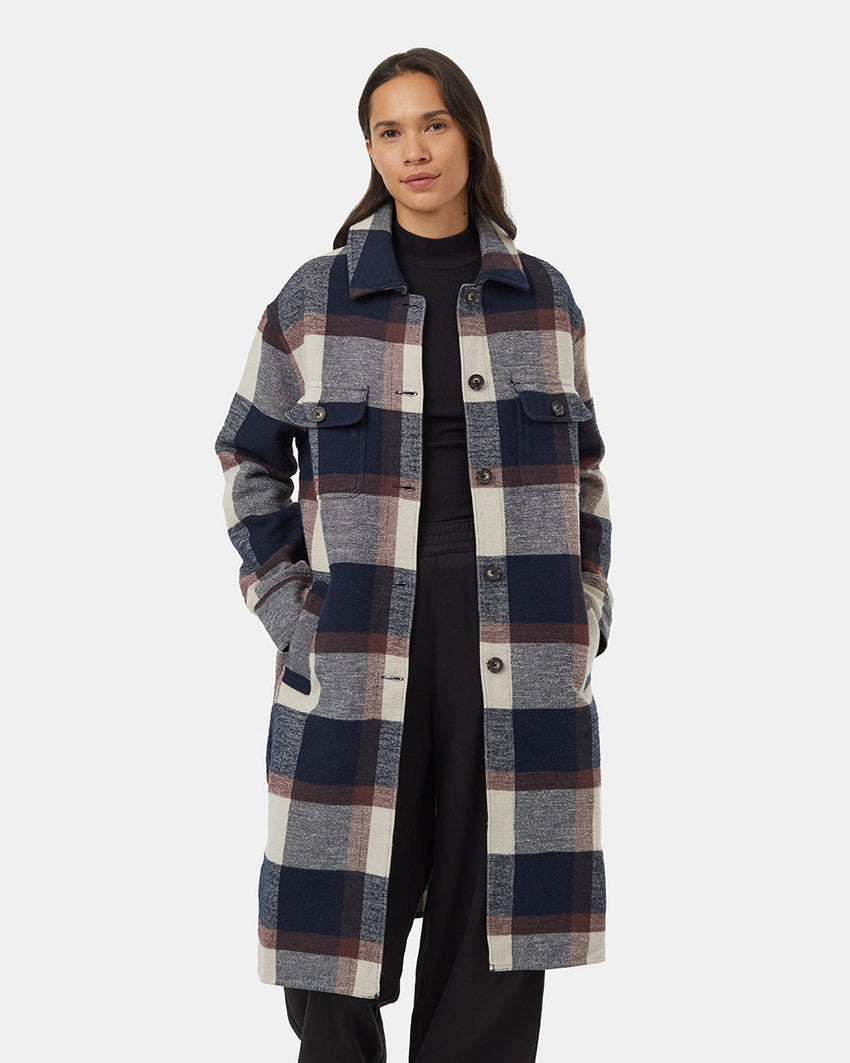 A person wearing the Tentree Heavy Weight Flannel Long Jacket made from recycled materials, featuring large blue, white, grey, and burgundy checks. With one hand in a pocket and the other resting by their side, they stand against a plain background with long hair flowing down.